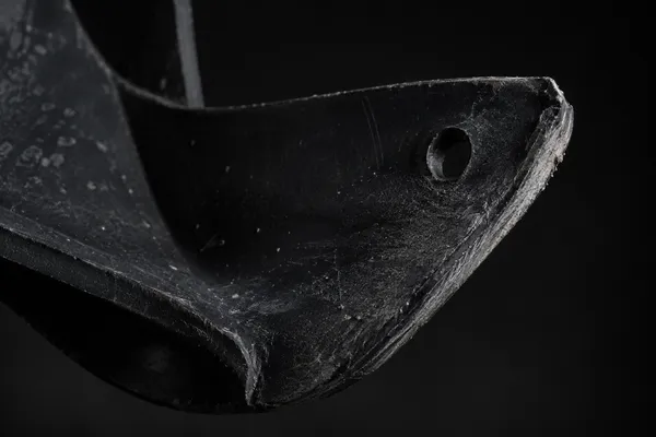 Extreme close view of a single black rubber rotor paddle from a single-stage snow blower with a curled thinned edge and a round wear-indicator hole near the tip.