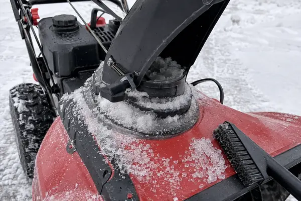 Close view of a red snow blower chute base with packed ice around the rotation joint and a clearing brush nearby.